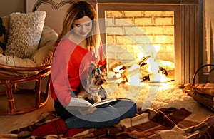 Woman with cute dog reading book near fireplace