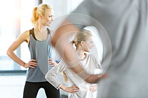 Woman and cute girl exercising with coach at fitness studio