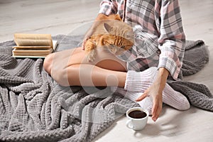 Woman with cute red cat and book on grey blanket at home, closeup. Space for text