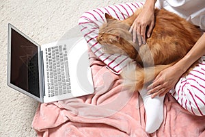 Woman with cute red cat and laptop on carpet at home