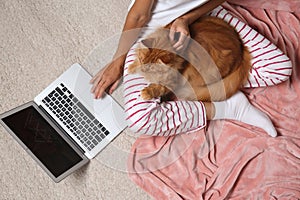 Woman with cute red cat and laptop on light carpet