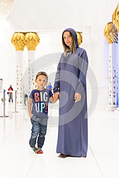 Woman with cute son dreaming at the grand mosque of Sheikh Zayed Mosque in Abu Dhabi wearing abaya, paranja in night time. Travell