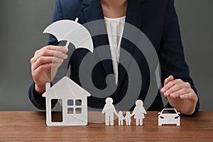 Woman with cutout paper family, house, car and umbrella at table, closeup.