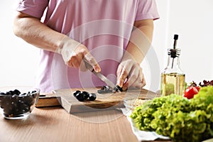 Woman cuts black olives. The process of making salad