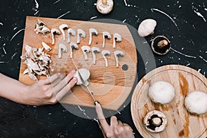 Woman cuts champignons on a cutting board with mushrooms. Hands of a girl with a knife and mushrooms on a dark background. Top