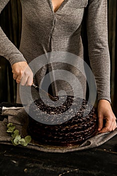 Woman cuts chocolate cake close. Dark tones