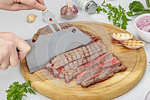 Woman cuts grilled steak. Female hands with knife and two pronged fork. Fresh herbs, vegetables