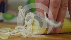 Woman cuts leek on wooden cutting board. A female chef uses a kitchen knife to chop the usual ingredient of soups and