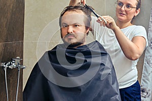 A woman cuts a man`s hair with scissors in the bathroom close up. The concept of grooming and problems with appearance when