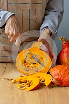 woman cuts orange pumpkins with a knife on a cutting board in the kitchen. cooking pumpkin is an eco-friendly food for