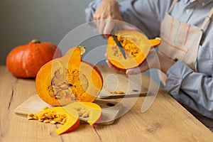 woman cuts orange pumpkins with a knife on a cutting board in the kitchen. cooking pumpkin is an eco-friendly food for