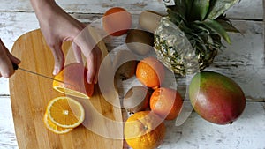 Woman cuts an orange on a wooden board. 4k top view