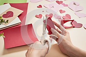 Woman cuts out red felt hearts, homemade crafts for Valentine`s day, hand made creativity, top view