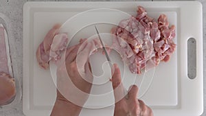 The woman cuts raw boneless skinless chicken thighs.