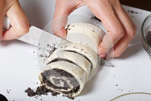 A woman cuts rolled puff pastry with a knife. Filled with poppy and walnuts. For making curls. Nearby on the table are ingredients