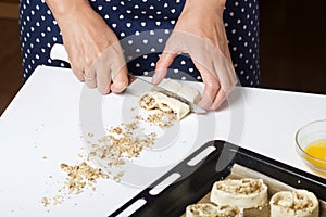 A woman cuts rolled puff pastry with a knife. Filled with poppy and walnuts. For making curls. Nearby on the table are ingredients