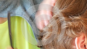 A woman cuts a teenager's haircut. Long curly light red hair cut with scissors close up view