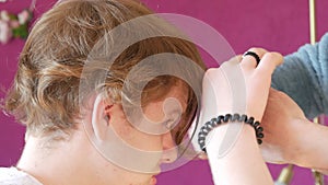 A woman cuts a teenager's haircut. Long curly light red hair cut with scissors and comb