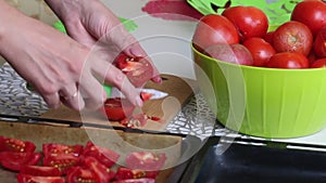 The woman cuts the tomatoes on a cutting board and puts them on a baking sheet. Cooking sun-dried tomatoes in olive oil. Close-up