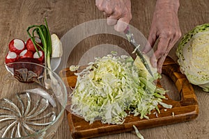 A woman cuts vegetables on a wooden cutting board for making vegetable salad from fresh raw vegetables cabbage, radish, green