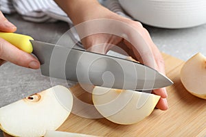 Woman cutting apple pear at grey table, closeup