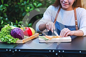A woman cutting and chopping carrot by knife on wooden board with mixed vegetables in a tray
