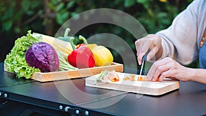 A woman cutting and chopping carrot by knife on wooden board with mixed vegetables in a tray