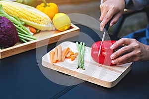 a woman cutting and chopping red bell pepers by knife on wooden board with mixed vegetables in a tray