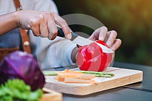 A woman cutting and chopping red bell pepers by knife on wooden board with mixed vegetables in a tray