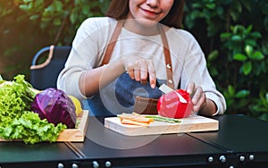 A woman cutting and chopping red bell pepers by knife on wooden board with mixed vegetables in a tray