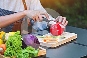 A woman cutting and chopping red bell pepers by knife on wooden board with mixed vegetables in a tray