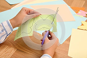 Woman cutting color paper with scissors at wooden table, closeup