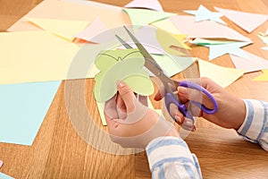 Woman cutting color paper with scissors at wooden table, closeup