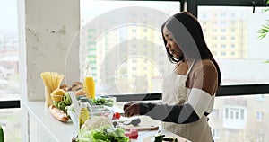 Woman cutting fresh cucumber in kitchen