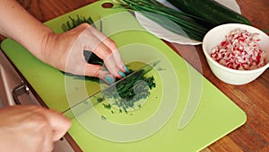 Woman is cutting fresh dill  in the kitchen on wooden table