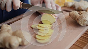 Woman cutting fresh ginger root on kitchen table, close up