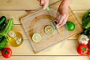 Woman cutting fresh green lime on wooden board