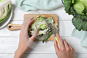 Woman cutting fresh green savoy cabbage at white wooden table