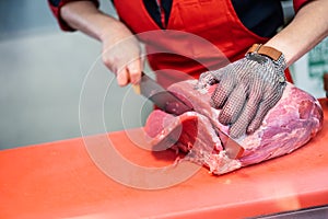 Woman cutting fresh meat in a butcher shop with metal safety mes