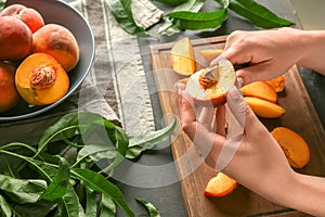 Woman cutting fresh peaches at grey table