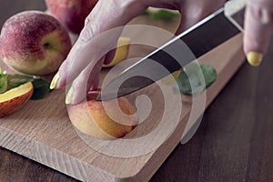 A woman cutting fresh peaches on a wooden cutting board, close up