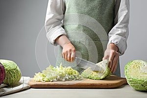 Woman cutting fresh savoy cabbage on board at wooden table, closeup