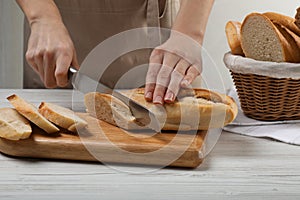 Woman cutting freshly baked baguette at white wooden table, closeup