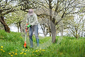 Woman is cutting grass by string trimmer in garden