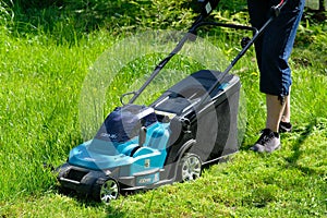 Woman cutting grass using electric lawn mower, close up view