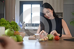 Woman cutting green apple on wooden board while preparing ingredients for making healthy food at home.