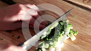 Woman is cutting green onion with knife on wooden board. Food ingredients salad