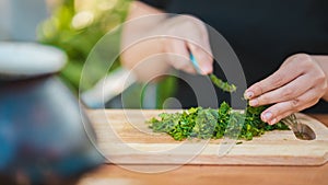 Woman cutting greens on wooden board outdoors. Close up of woman`s hands cutting verdure with knife on chopping board