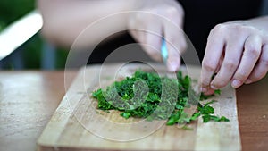 Woman cutting greens on wooden board outdoors. Close up of woman's hands cutting verdure with knife on chopping board