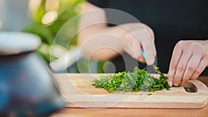 Woman cutting greens on wooden board outdoors. Close up of woman& x27;s hands cutting verdure with knife on chopping board.